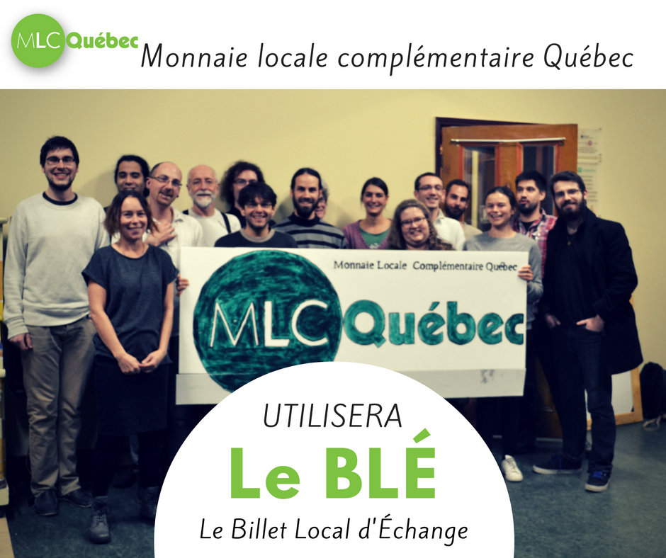 Photo avec l'ajout des mots Le BLÉ : Billet Local d'Échange. Une vingtaine de personnes posent en groupe lors de l'assemblée constituante, tentant une bannière MLC Québec.